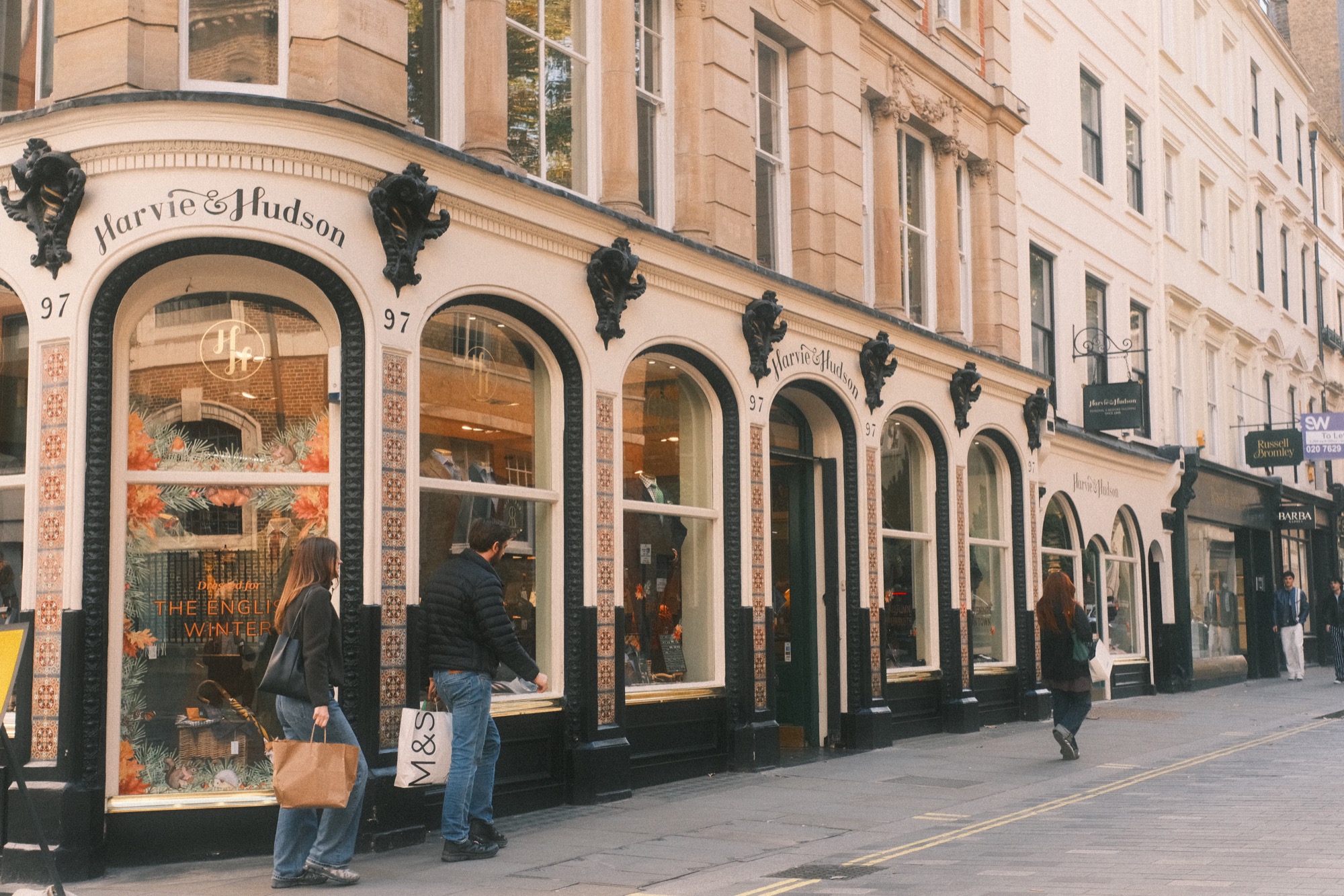 Two shoppers pass the arched windows of Harvie & Hudson on Jermyn Street.