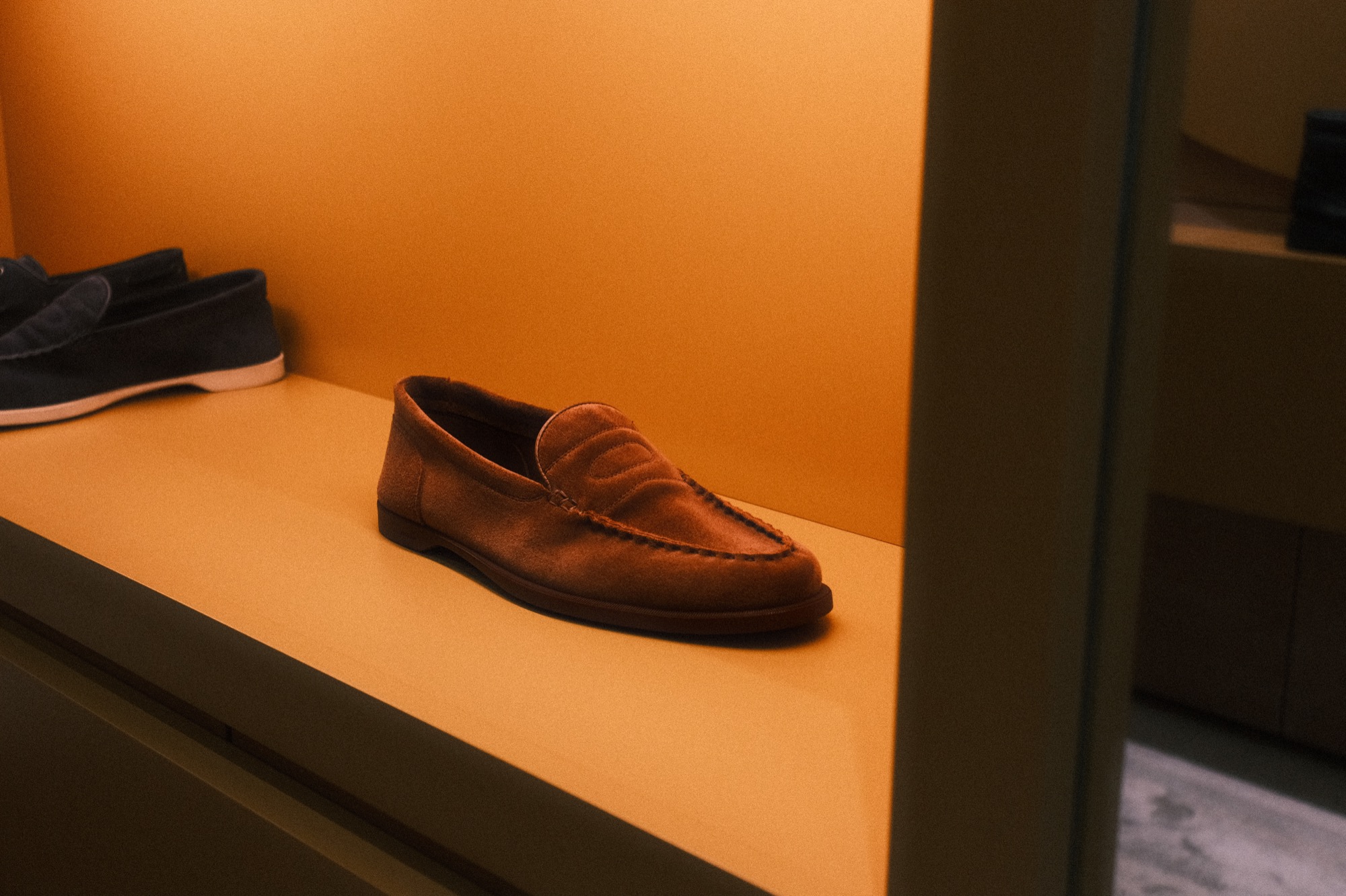 A loafer on a lit shelf in the John Lobb window, in orange light.